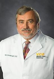 Man with gray hair and facial hair wearing a white lab coat