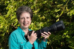 Ann Fulcher in green shirt holding a camera with large lens
