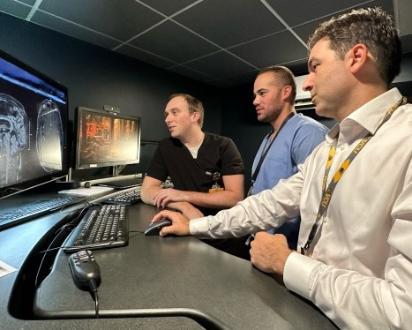 Three male physicians at a standing desk looking at a medical image of a head