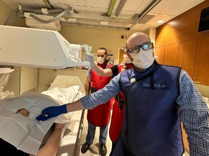 Three men standing next to C T scanner and all wearing red lead aprons