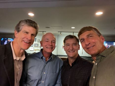 Four male radiology alumni in button up shirts standing together smiling